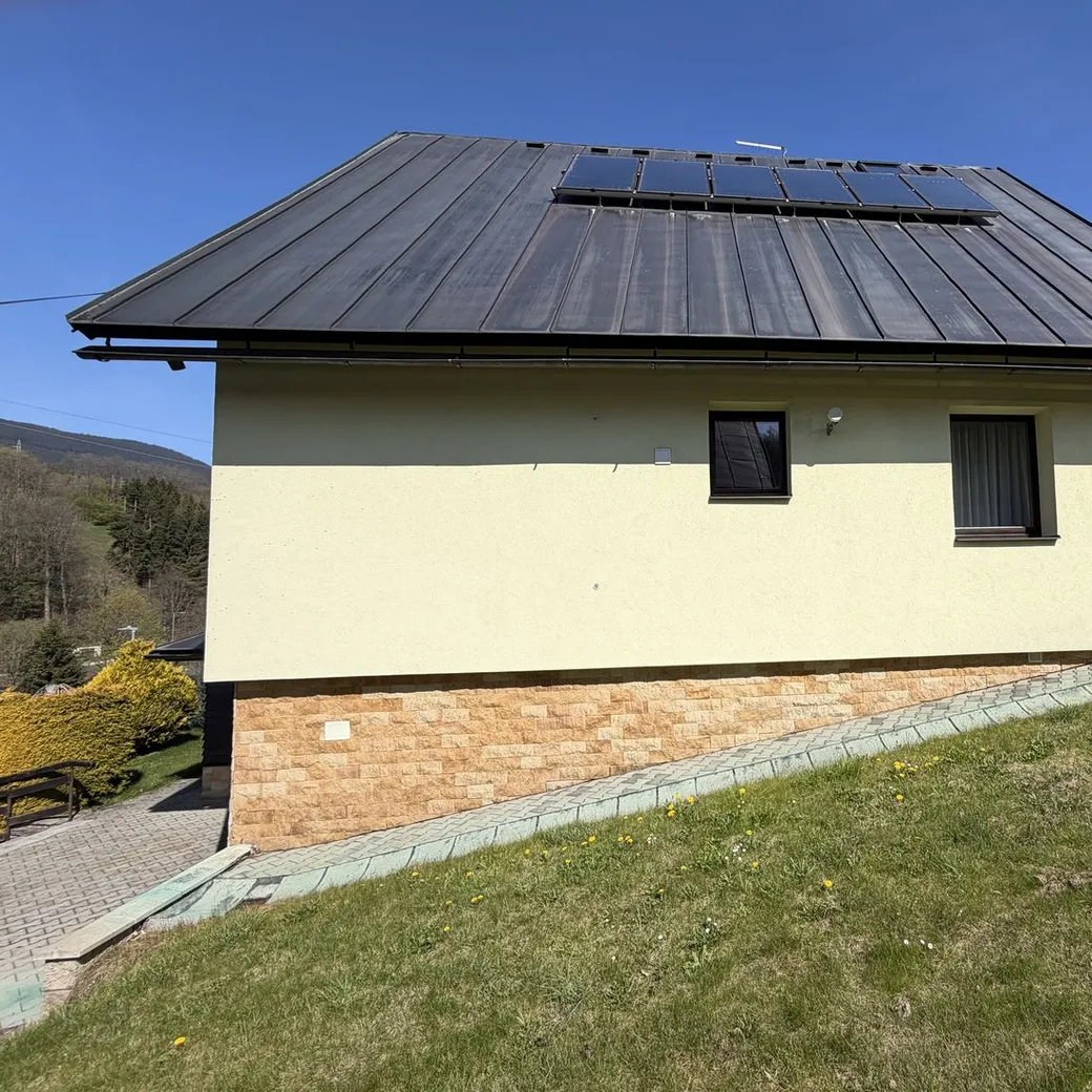 Boční pohled na rodinný dům s kamenným soklem, zaměřovaný objekt